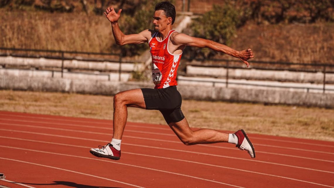 Energetic athlete captured mid-jump during a track event, showcasing strength and agility.