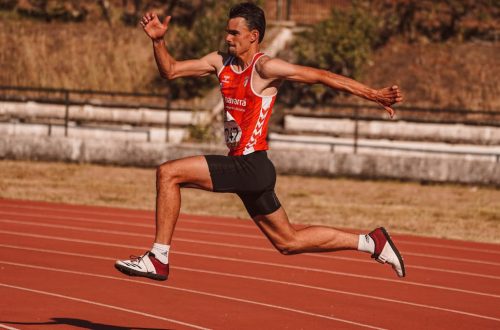 Energetic athlete captured mid-jump during a track event, showcasing strength and agility.