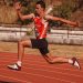 Energetic athlete captured mid-jump during a track event, showcasing strength and agility.